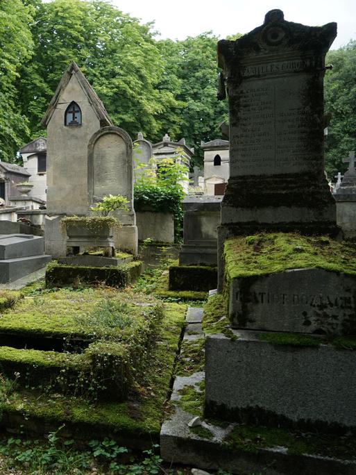 Das Bild zeigt mehrere Gräber und Gruften auf dem Pariser Friedhof Père-Lachaise, die teilweise stark mit Moos bewachsen sind. 