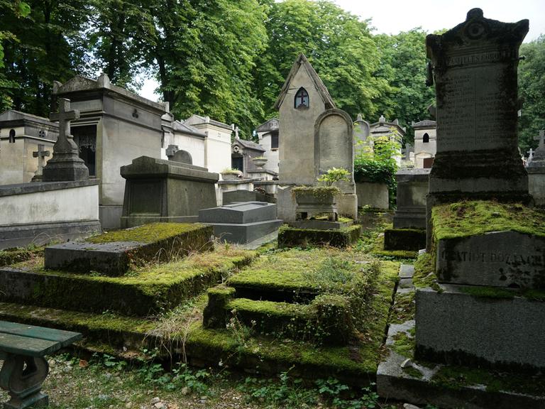 Das Bild zeigt mehrere Gräber und Gruften auf dem Pariser Friedhof Père-Lachaise, die teilweise stark mit Moos bewachsen sind. 