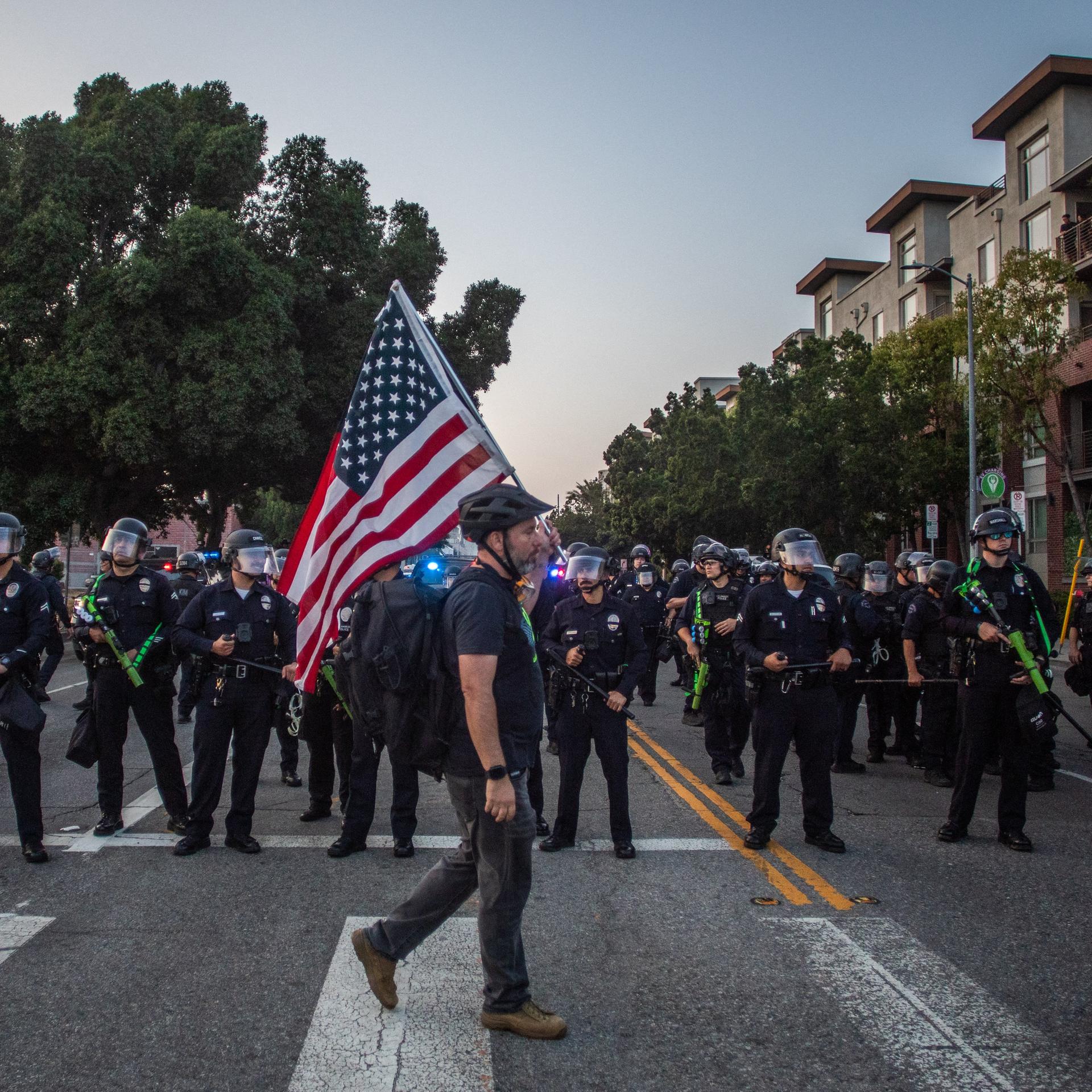 Ein Mann mit US-Flagge läuft in Los Angeles an Polizisten vorbei Ein Mann mit US-Flagge läuft in Los Angeles an Polizisten vorbei