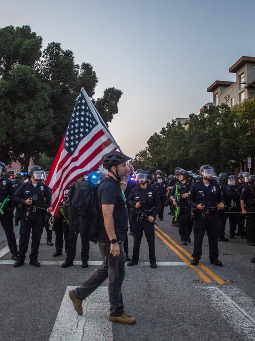Ein Mann mit US-Flagge läuft in Los Angeles an Polizisten vorbei