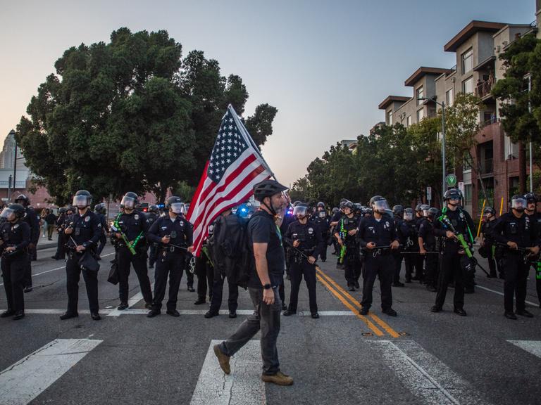 Ein Mann mit US-Flagge läuft in Los Angeles an Polizisten vorbei