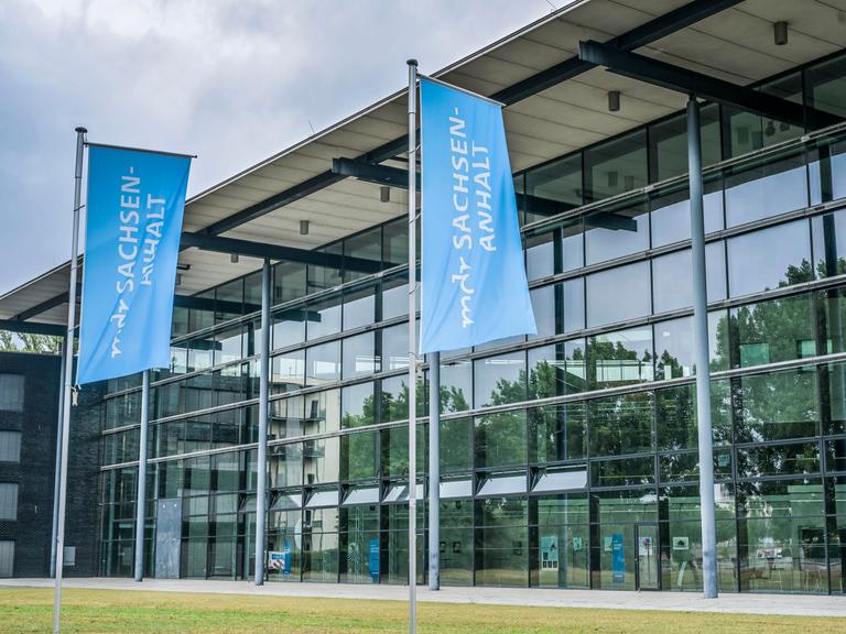 Blick auf das gläserne MDR-Landesfunkhaus in Magdeburg. Davor blaue Flaggen mit der Aufschrift "mdr Sachsen-Anhalt" Blick auf das gläserne MDR-Landesfunkhaus in Magdeburg. Davor blaue Flaggen mit der Aufschrift "mdr Sachsen-Anhalt"