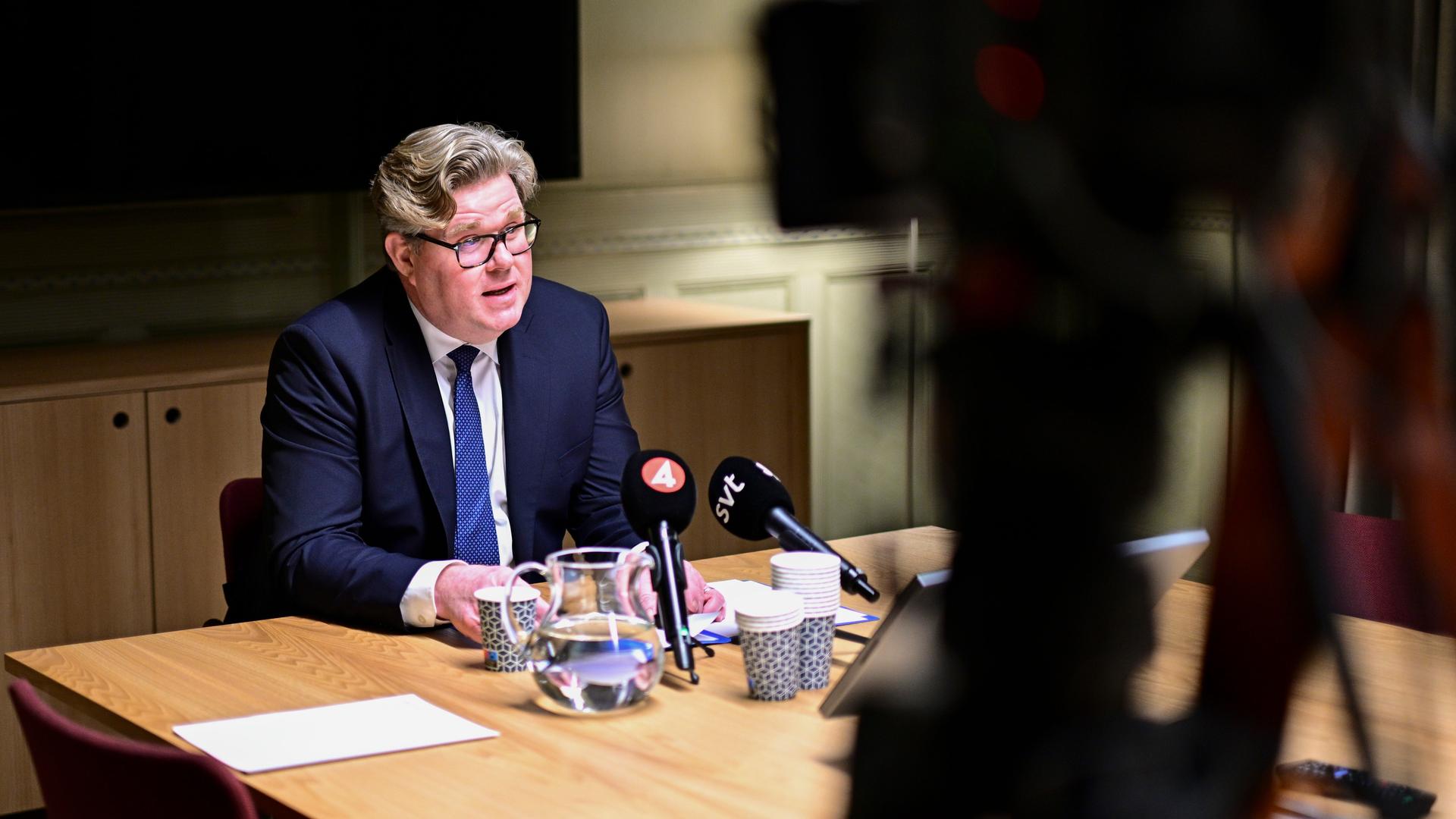 Der schwedische Justizminister Strömmer sitzt an einem Tisch hinter Mikrofonen. Darauf ist noch eine Wasserkaraffe und Becher zu sehen. Im Vordergrund verschwommen eine Kamera. Der schwedische Justizminister Strömmer sitzt an einem Tisch hinter Mikrofonen. Darauf ist noch eine Wasserkaraffe und Becher zu sehen. Im Vordergrund verschwommen eine Kamera.