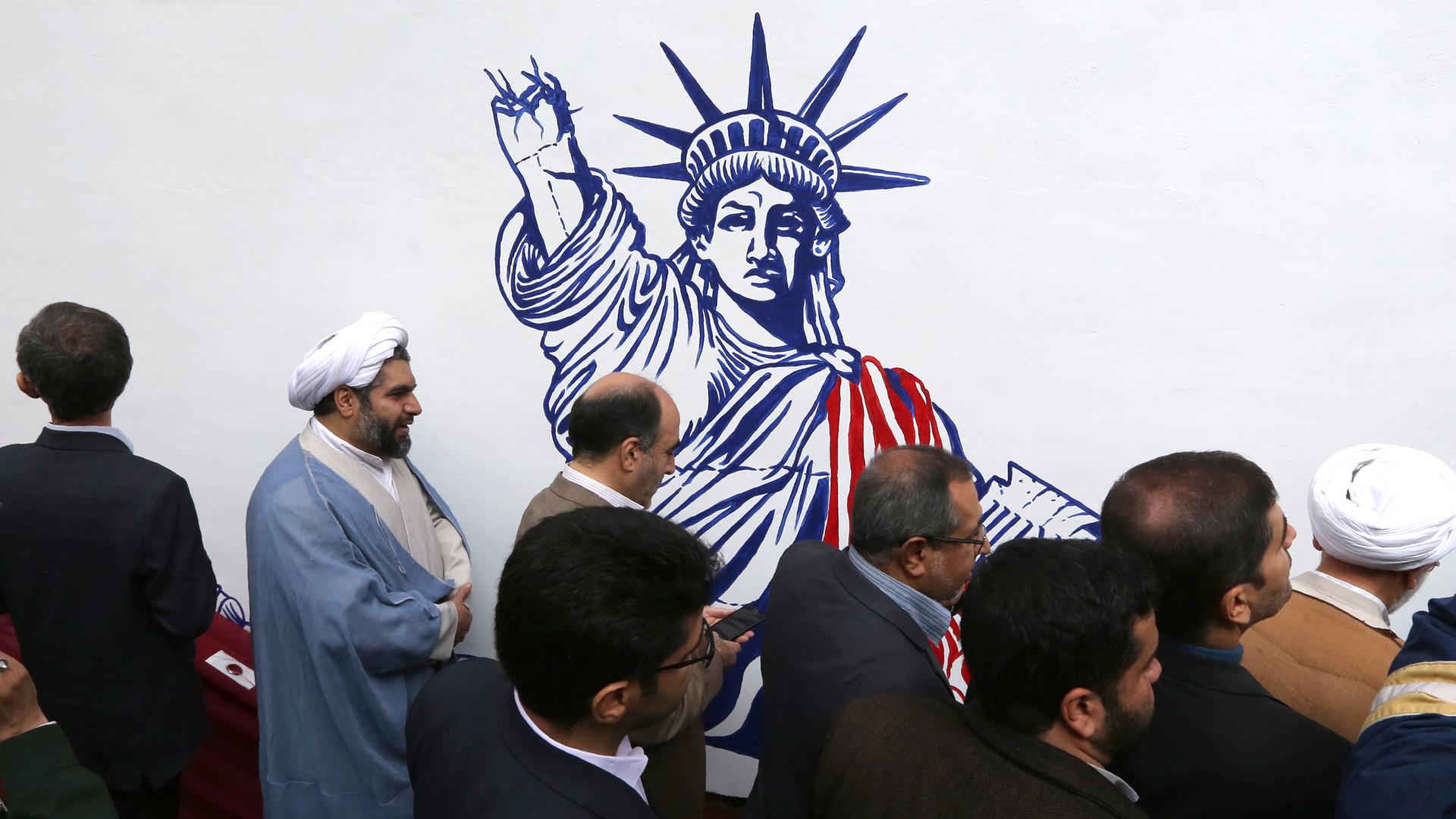 Iranische Männer vor dem Wandgemälde an der ehemaligen US-Botschaft in der Hauptstadt Teheran, die Freiheitsstatue wird mit abgehacktem Arm gezeigt.