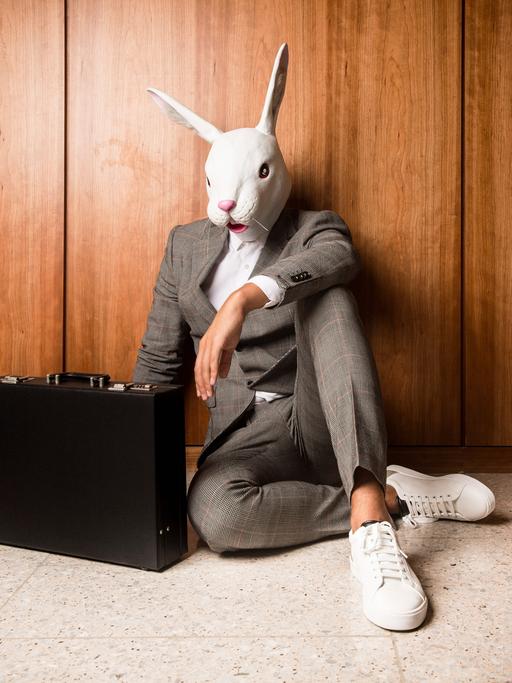 Ein Businessmann im Anzug und Aktenkoffer mit einer weißen Hasenmaske auf dem Kopf.