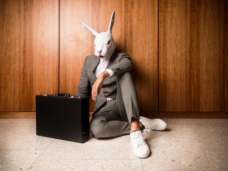 Ein Businessmann im Anzug und Aktenkoffer mit einer weißen Hasenmaske auf dem Kopf.