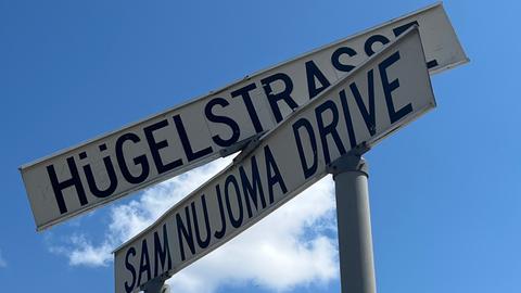 Zwei Schilder markieren eine Kreuzung in Windhoek. Eine Straße ist nach Sam Nujoma benannt, dem Staatsgründer von Namibia, auf dem anderen Schild steht auf Deutsch Hügelstraße