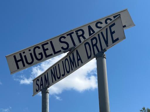 Zwei Schilder markieren eine Kreuzung in Windhoek. Eine Straße ist nach Sam Nujoma benannt, dem Staatsgründer von Namibia, auf dem anderen Schild steht auf Deutsch Hügelstraße
