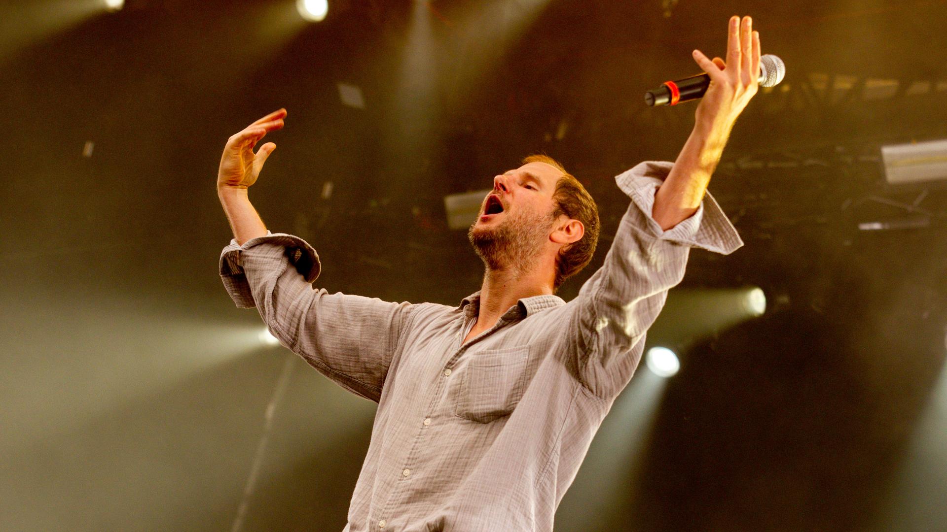 Marco Wanda steht bei einem Konzert auf der Bühne, die Arme in die Luft gestreckt.