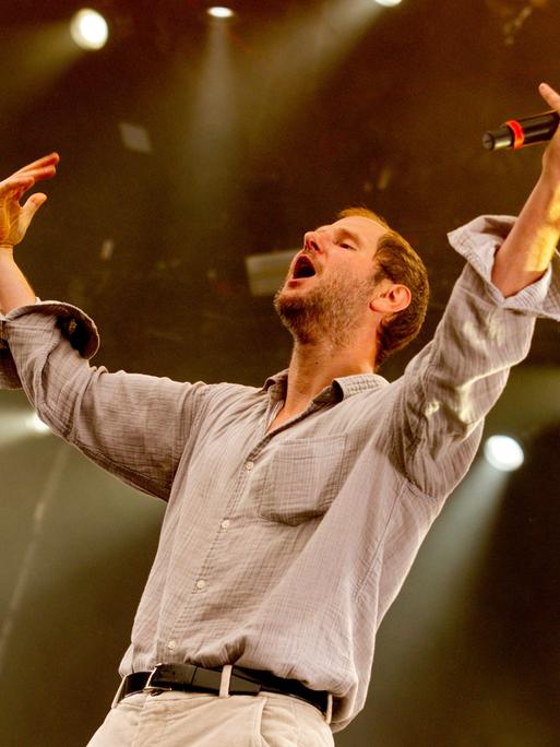 Marco Wanda steht bei einem Konzert auf der Bühne, die Arme in die Luft gestreckt.