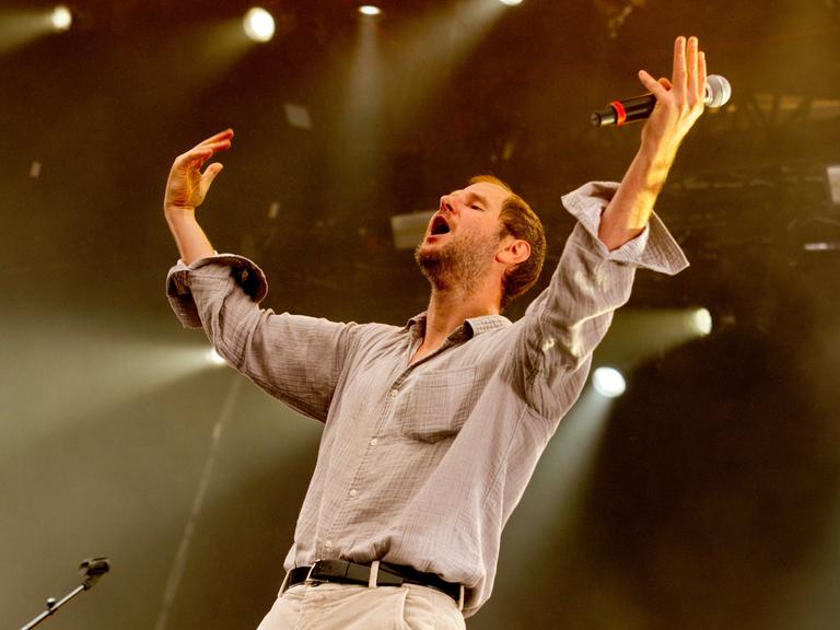 Marco Wanda steht bei einem Konzert auf der Bühne, die Arme in die Luft gestreckt.