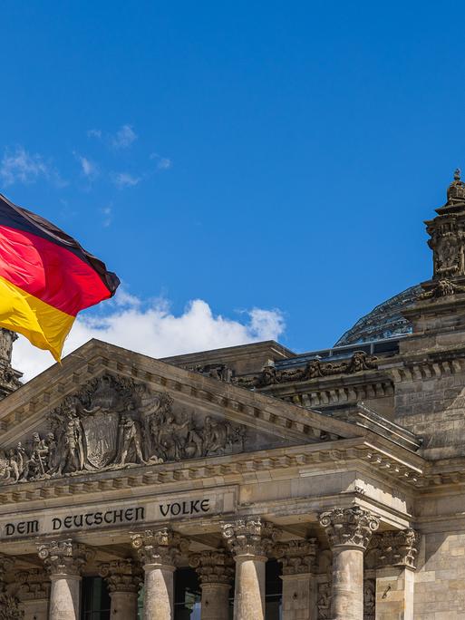 Die deutsche Nationalflagge weht vor dem Reichstagsgebäude in Berlin, Deutschland. Im Hintergrund ist die markante Glaskuppel des Parlamentsgebäudes zu sehen.