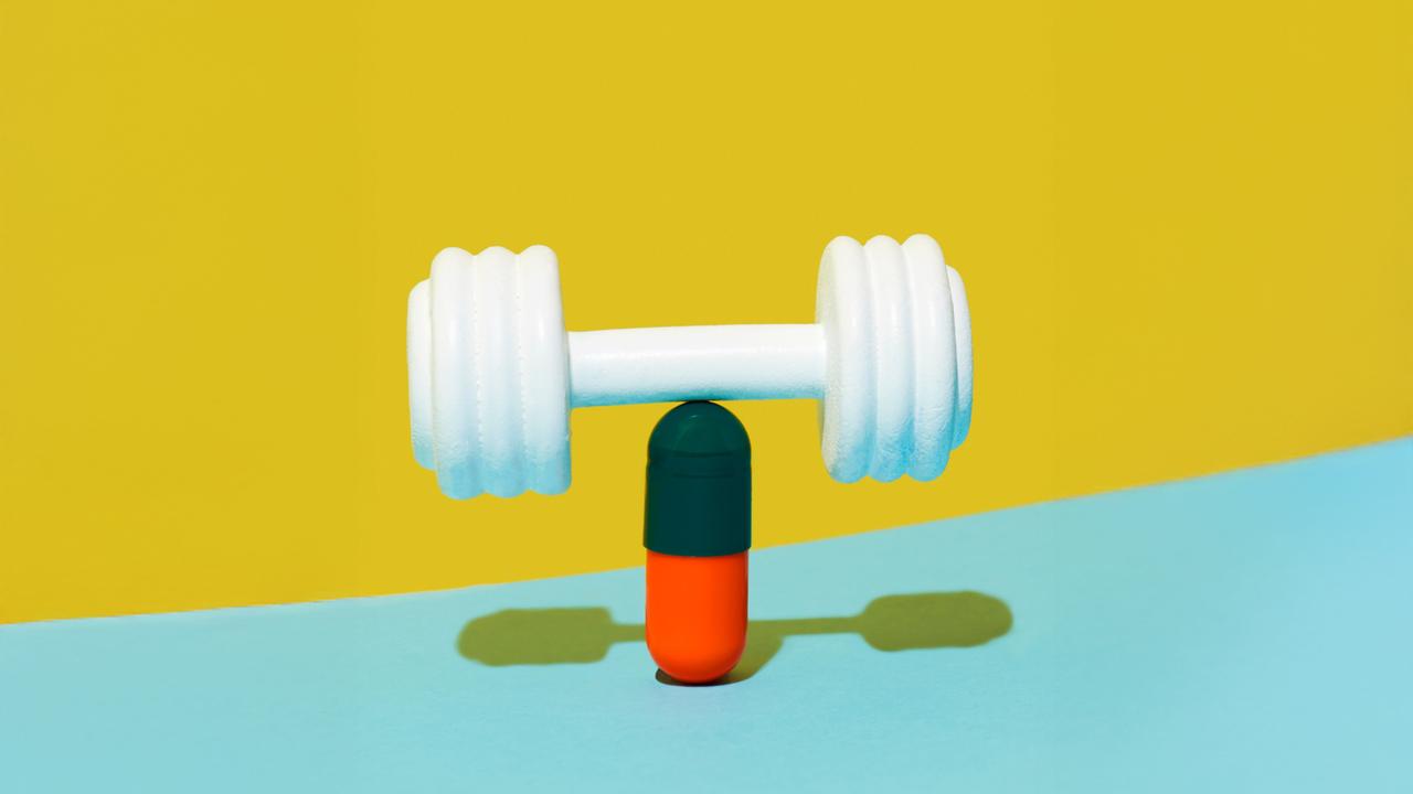 Eine weiße Hantel balanchiert auf einer grünroten Pille auf einem gelben und blauen Hintergrund.