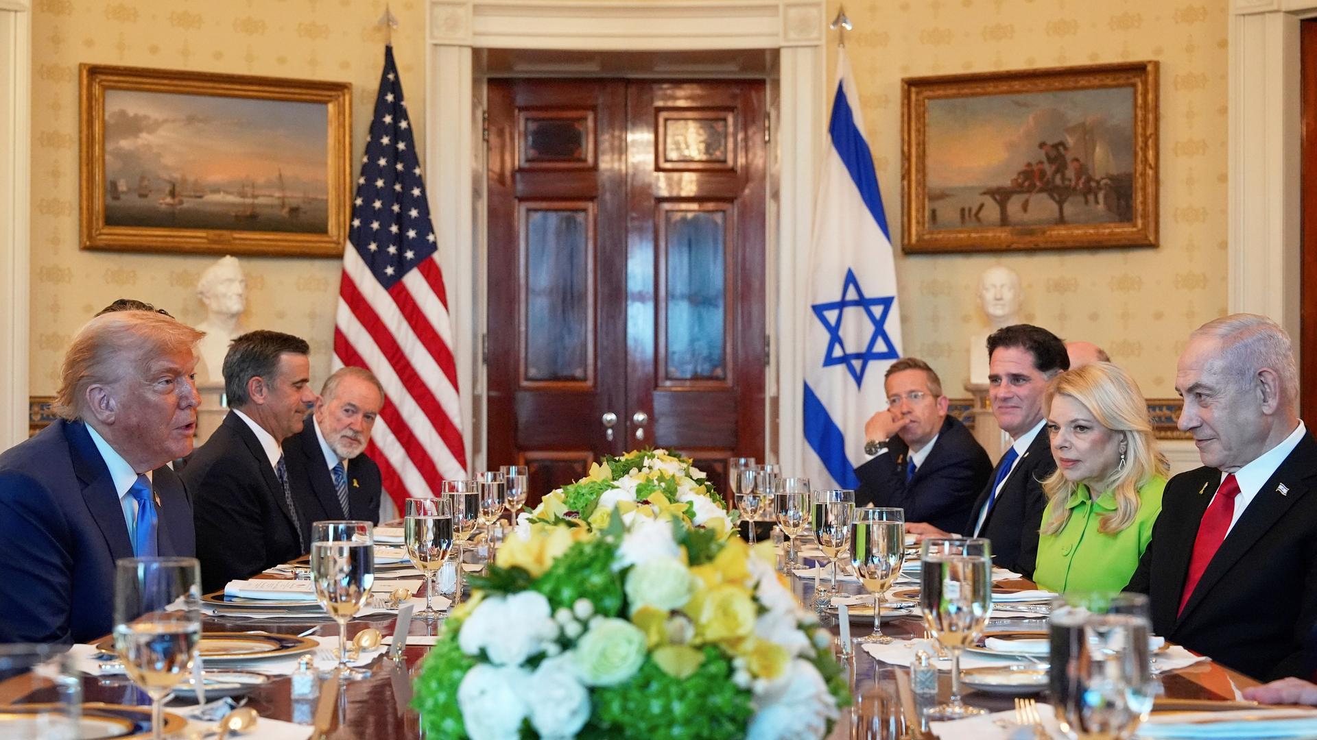 Donald Trump und Benjamin Netanjahu sitzen zusammen mit anderen Personen an einem festlich gedeckten Tisch im Weißen Haus.