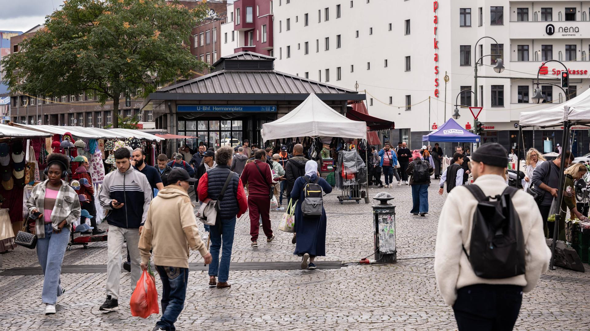 Passanten laufen an den Marktständen am Berliner Hermannplatz vorbei. Im Hintergrund der Zugang zur U-Bahn-Haltestelle.  Passanten laufen an den Marktständen am Berliner Hermannplatz vorbei. Im Hintergrund der Zugang zur U-Bahn-Haltestelle.