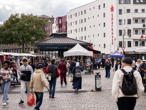 Passanten laufen an den Marktständen am Berliner Hermannplatz vorbei. Im Hintergrund der Zugang zur U-Bahn-Haltestelle. 