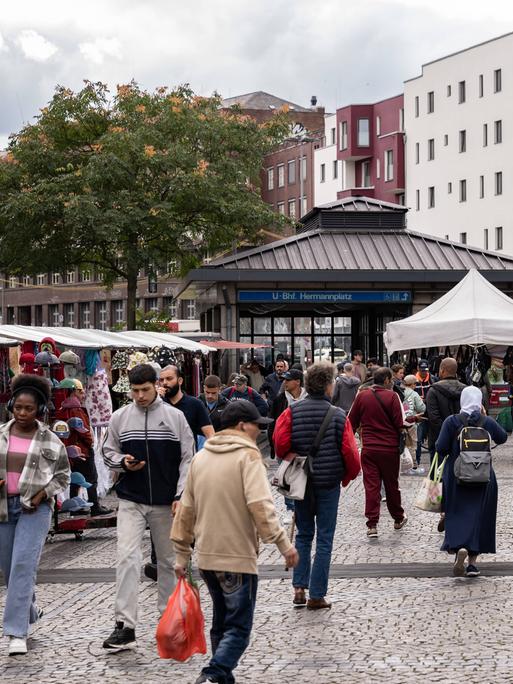 Passanten laufen an den Marktständen am Berliner Hermannplatz vorbei. Im Hintergrund der Zugang zur U-Bahn-Haltestelle. 