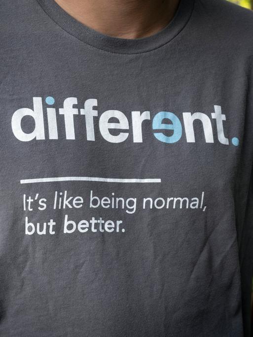 "Anders ist so wie Normalsein – nur besser," steht in weißen Buchstaben auf Englisch auf dem dunkelgrauen T-Shirt eines jungen Mannes. 