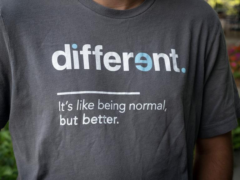 "Anders ist so wie Normalsein – nur besser," steht in weißen Buchstaben auf Englisch auf dem dunkelgrauen T-Shirt eines jungen Mannes. 
