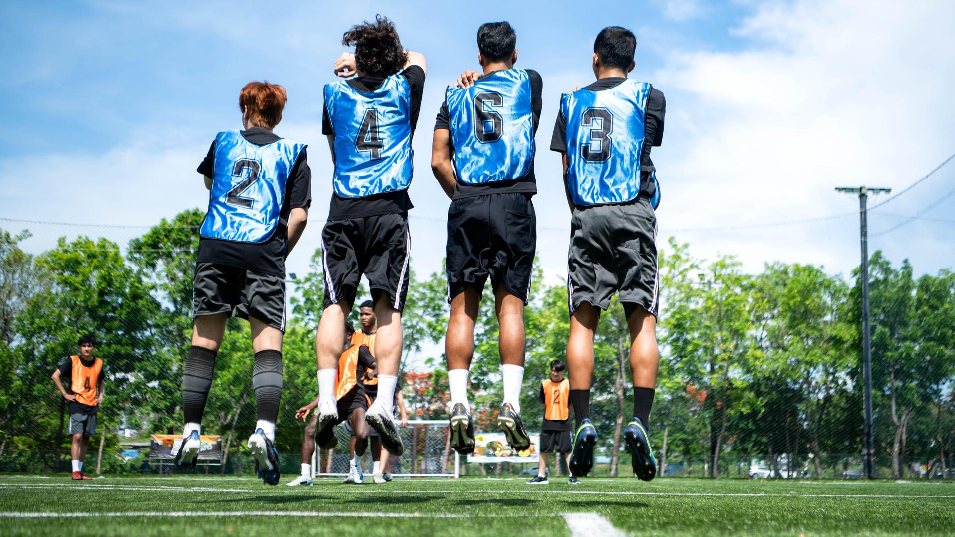 Junge Fußballspieler springen beim Training nebeneinander vor dem Tor in die Höhe, um Verteidigungstaktiken zu üben.
