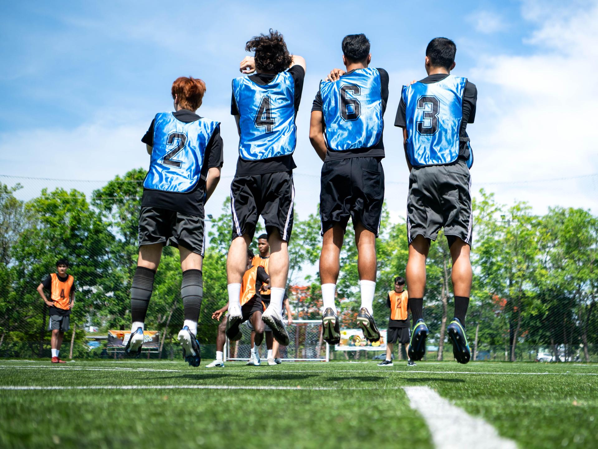 Junge Fußballspieler springen beim Training nebeneinander vor dem Tor in die Höhe, um Verteidigungstaktiken zu üben.