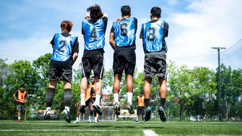 Junge Fußballspieler springen beim Training nebeneinander vor dem Tor in die Höhe, um Verteidigungstaktiken zu üben.