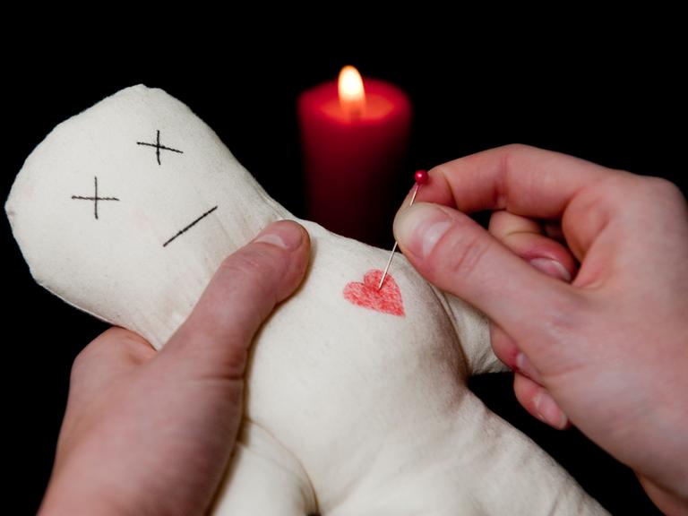 ILLUSTRATION: Eine Frau steckt steckt eine Nadel ins Herz einer Voodoo-Puppe.