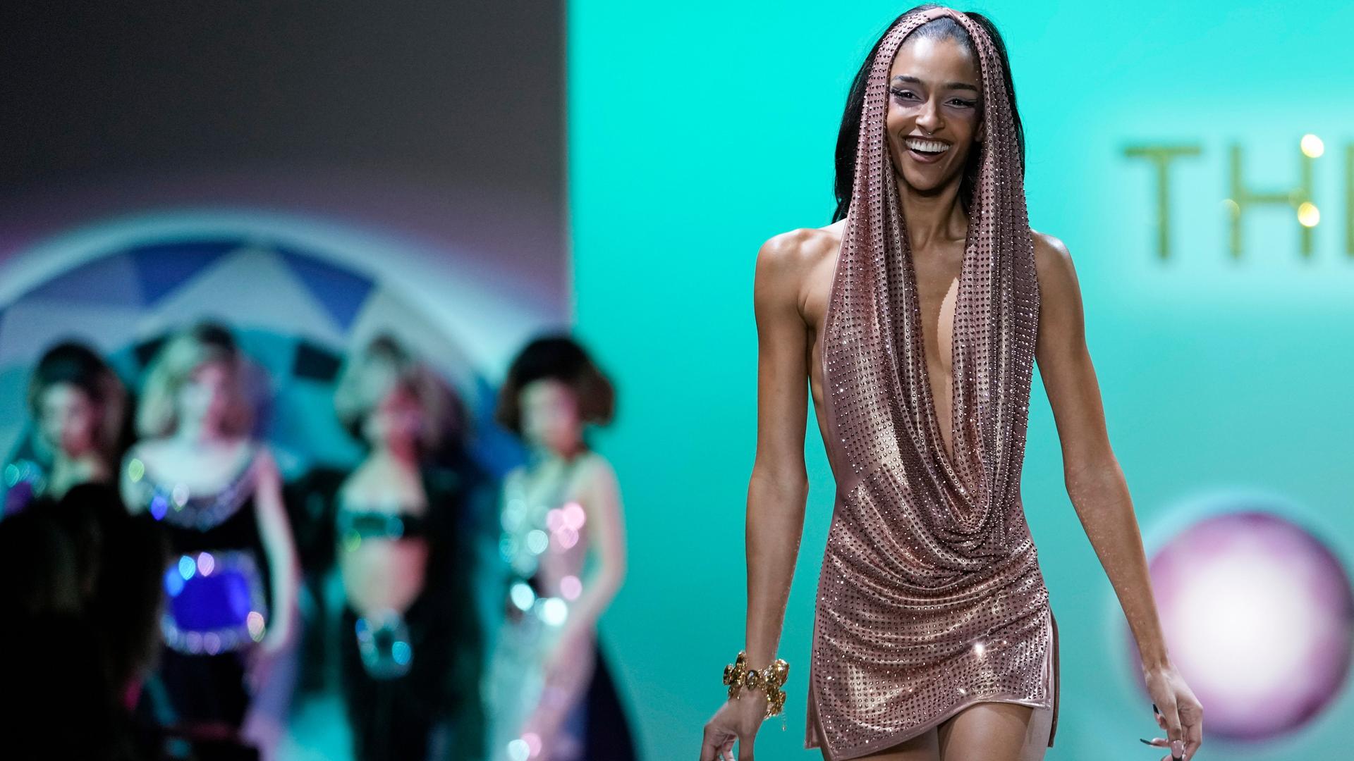 Ein weibliches Model läuft bei der Fashion Week in New York lächelnd über einen Laufsteg.