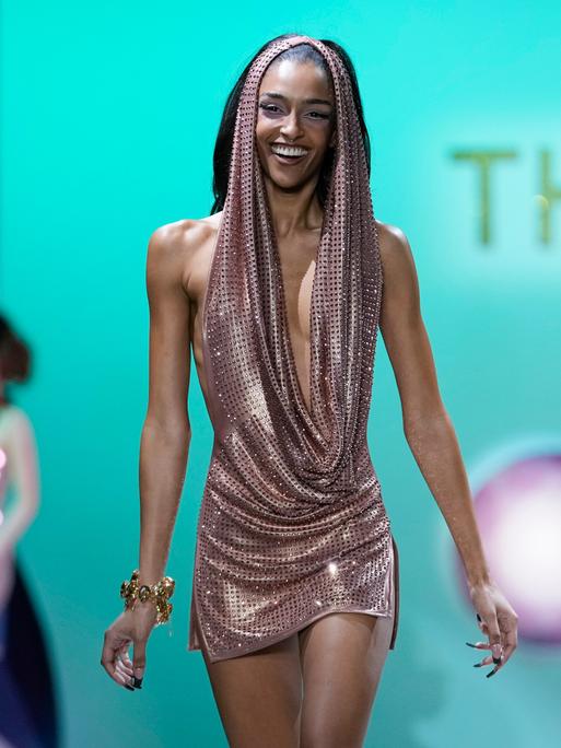 Ein weibliches Model läuft bei der Fashion Week in New York lächelnd über einen Laufsteg.