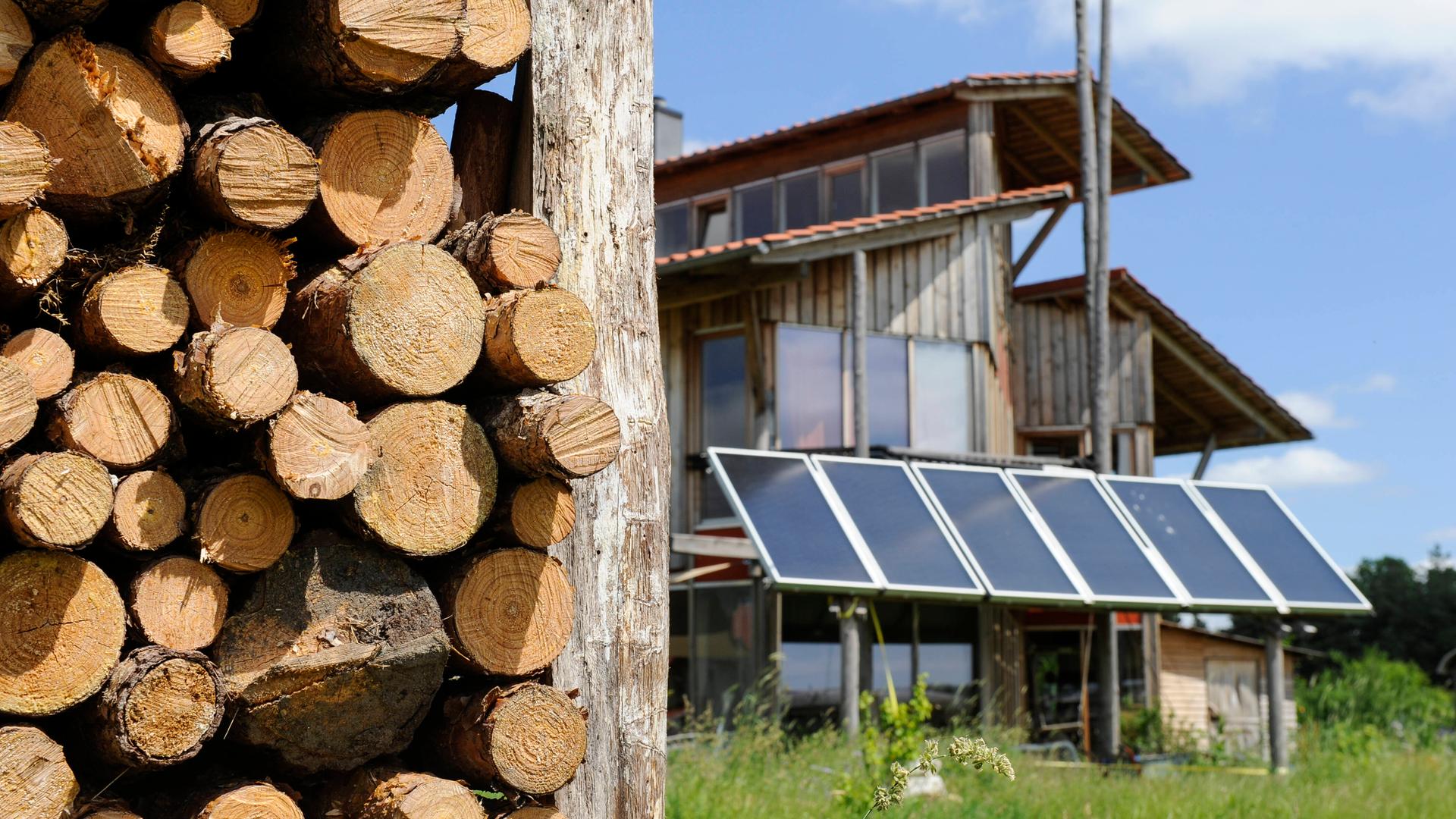 Wohnhaus aus Holz mit Sonnenkollektoren für Heizung und Warmwasser. Im Vordergrund ein Holzstapel.