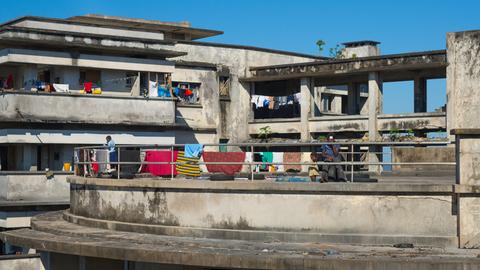 Blick auf die Ruine eines Hotels, auf dessen Balkonen Menschen zu sehen sind und auf dessen Brüstungen bunte Handtücher hängen. Blick auf die Ruine eines Hotels, auf dessen Balkonen Menschen zu sehen sind und auf dessen Brüstungen bunte Handtücher hängen.