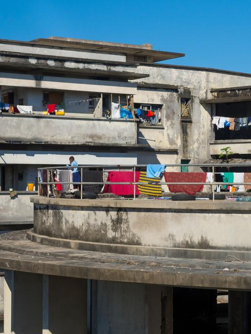 Blick auf die Ruine eines Hotels, auf dessen Balkonen Menschen zu sehen sind und auf dessen Brüstungen bunte Handtücher hängen.