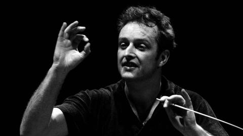 Der Dirigent Carlos Kleiber steht vor dem Orchester und dirigiert.