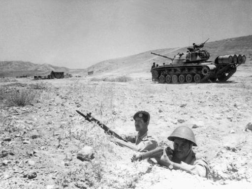 Zwei jordanische Soldaten beziehen bewaffnet Stellung an der Grenze zu Israel. Im Hintergrund ist ein Panzer zu sehen.