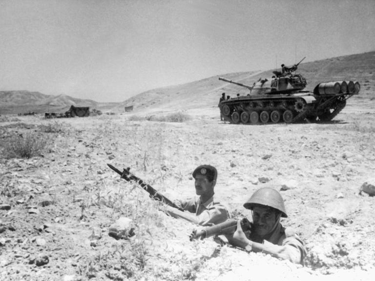 Zwei jordanische Soldaten beziehen bewaffnet Stellung an der Grenze zu Israel. Im Hintergrund ist ein Panzer zu sehen.
