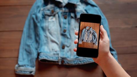 Eine Person nimmt mit einem Smartphone das Bild einer gebrauchten Jeansjacke auf.