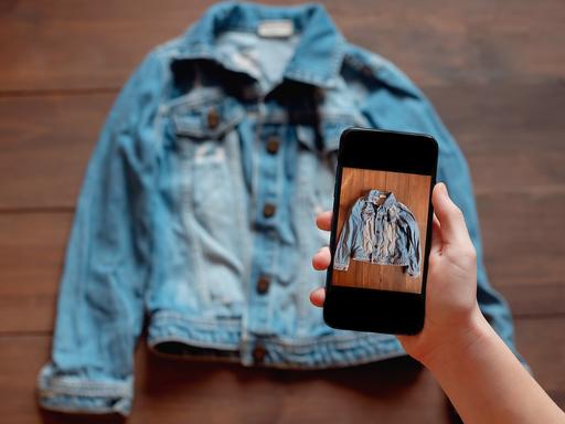 Eine Person nimmt mit einem Smartphone das Bild einer gebrauchten Jeansjacke auf. Eine Person nimmt mit einem Smartphone das Bild einer gebrauchten Jeansjacke auf.