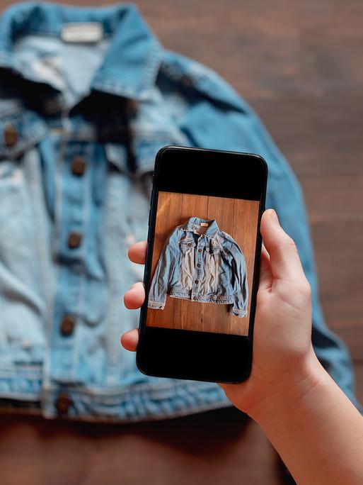 Eine Person nimmt mit einem Smartphone das Bild einer gebrauchten Jeansjacke auf. Eine Person nimmt mit einem Smartphone das Bild einer gebrauchten Jeansjacke auf.
