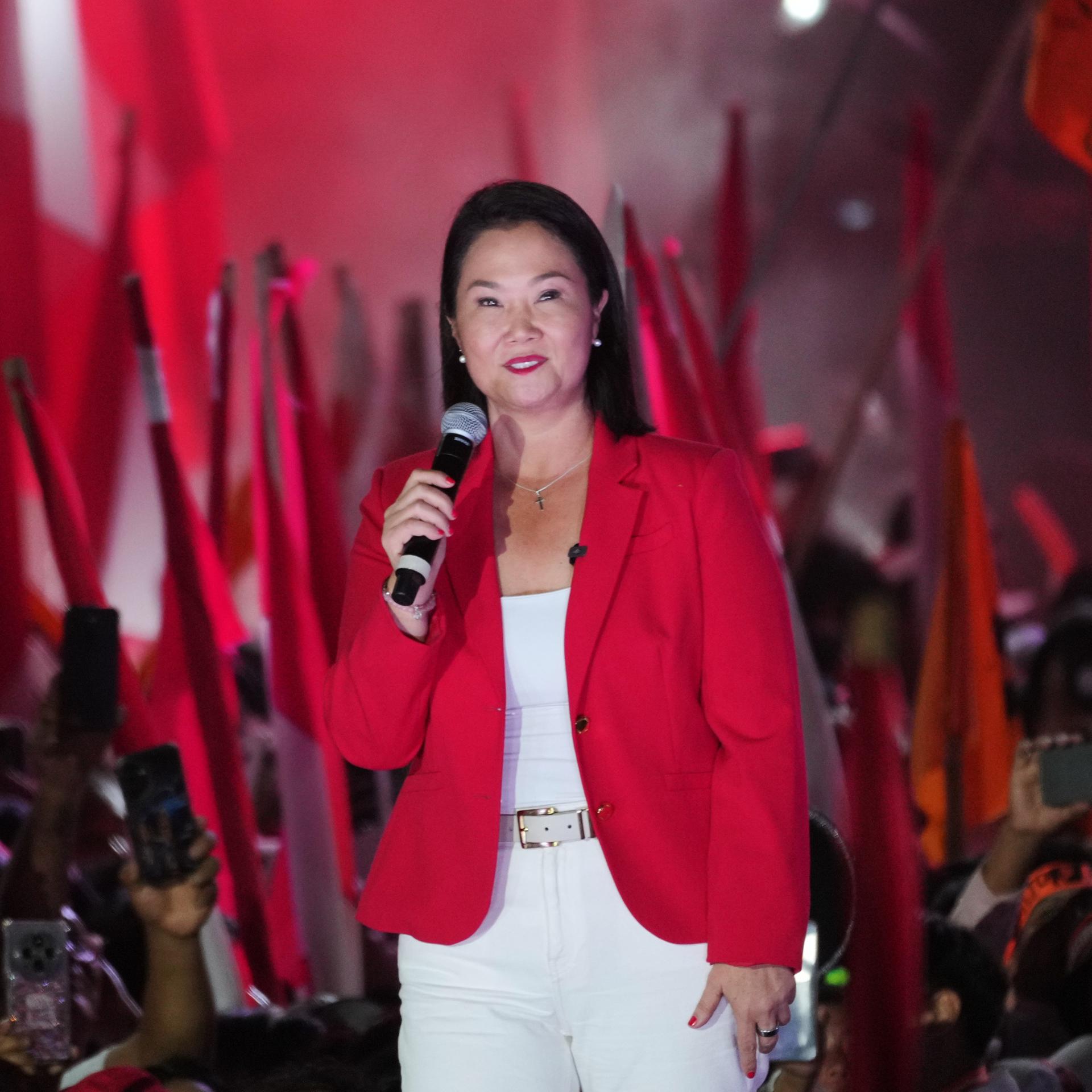 Keiko Fujimori hält ein Mikrofon in der Hand. Sie ist in den Farben rot und weiß gekleidet und steht erhöht. Hinter ihr sind viele Menschen, viele Flaggen in rot und weiß und roter Rauch. 