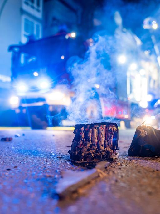Auf einer nächtlichen Straße liegt abgebranntes Feuerwerk, dahinter steht ein Feuerwehrauto.