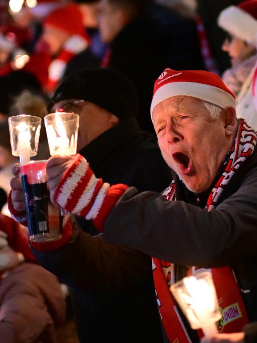 Weihnachtssingen im Stadion von Union Berlin. Ein Mann mit einer Nikolausmütze singt lauthals mit. 