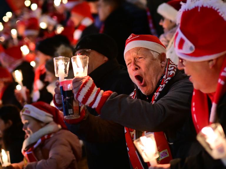 Weihnachtssingen im Stadion von Union Berlin. Ein Mann mit einer Nikolausmütze singt lauthals mit. 