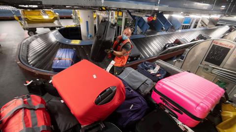 Ein Arbeiter hebt im Gepäckverteiler des Stuttgarter Flughafens einen Koffer von einem Gepäckband auf einen Transportwagen.