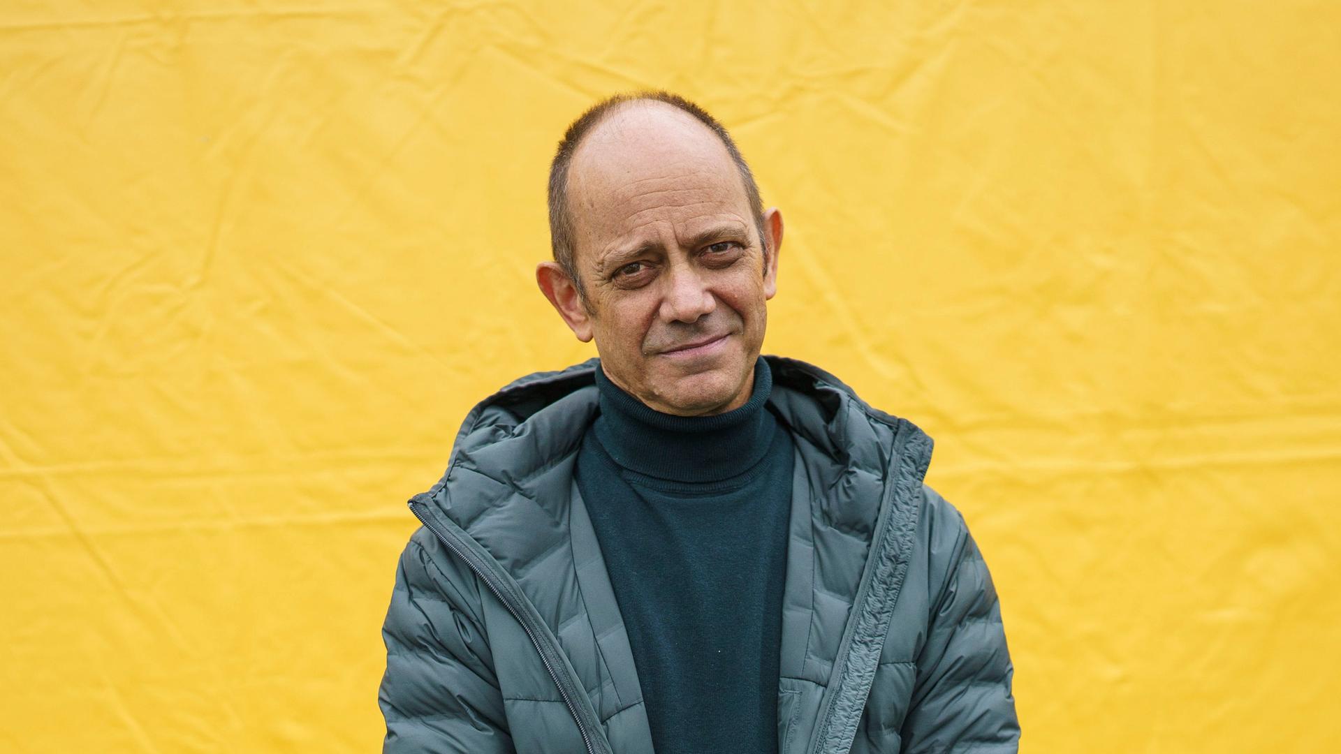 Der Schriftsteller Damon Galgut steht mit verschränkten Armen vor einer gelben Plane und blickt freundlich in die Kamera. Der Schriftsteller Damon Galgut steht mit verschränkten Armen vor einer gelben Plane und blickt freundlich in die Kamera.