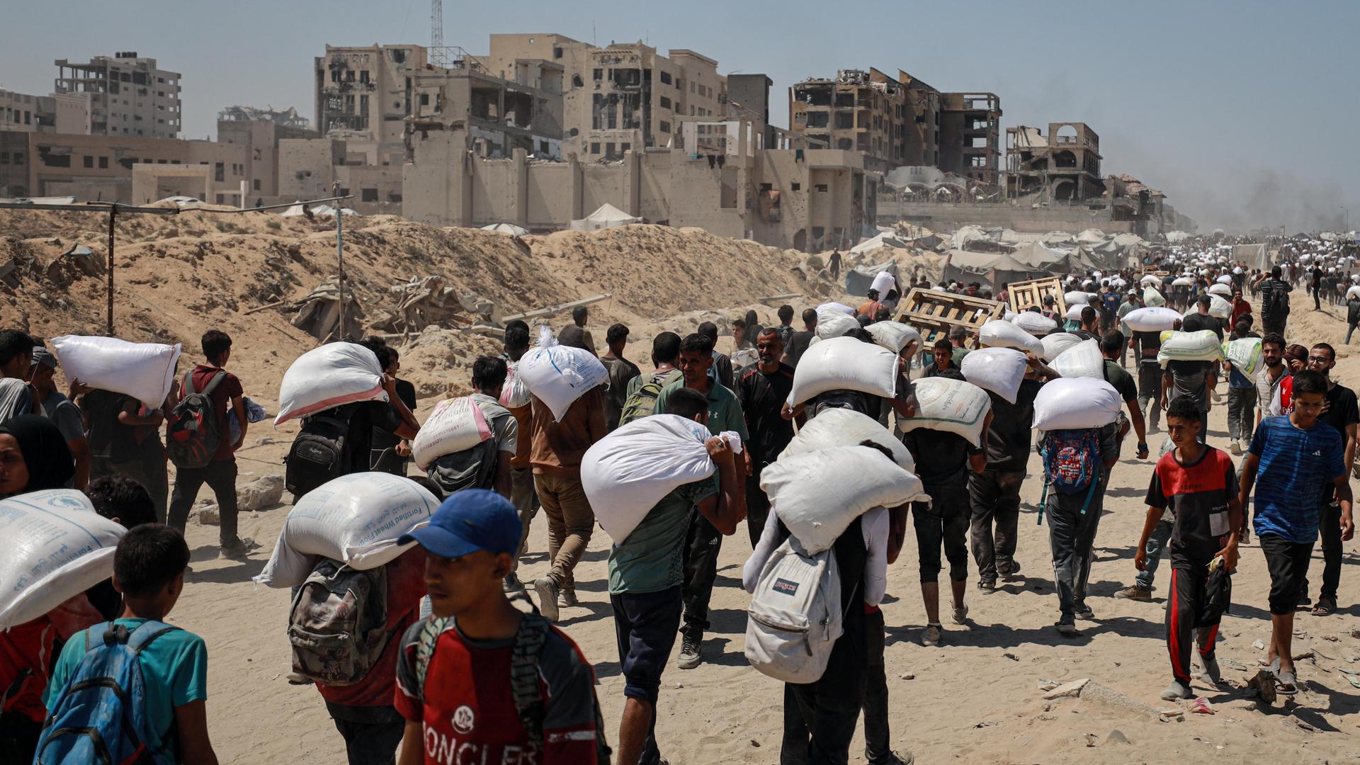 Menschen im Gaza-Streifen gehen hintereinander her. Sie tragen weiße Säcke. Menschen im Gaza-Streifen gehen hintereinander her. Sie tragen weiße Säcke.