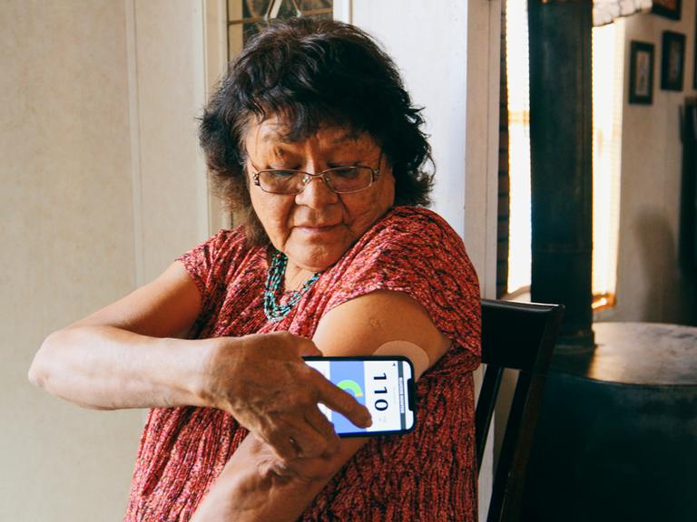 Eine ältere indigene Navajo-Frau, die ihren Blutzuckerspiegel mit einer Smartphone-Anwendung überprüft.
