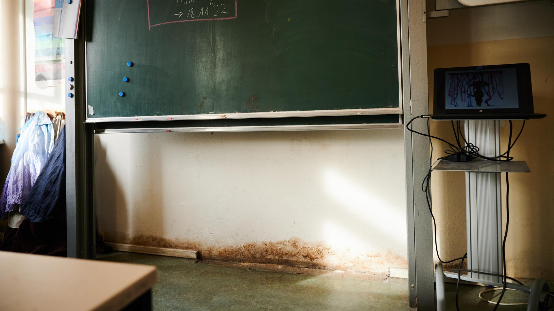 Blick in einen Klassenraum mit einer Tafel und Schimmel an der Wand.