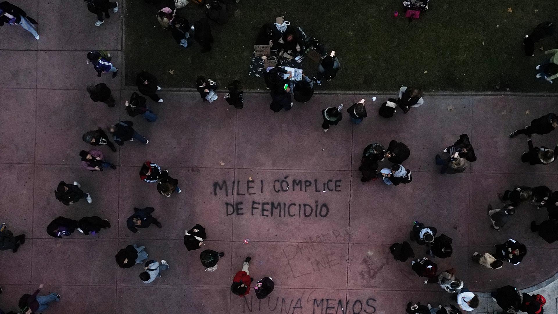 Argentinien, Buenos Aires: Demonstranten gehen in der Nähe eines Gemäldes mit der spanischen Aufschrift "Milei femicide accomplice" (Milei Frauenmord Mittäter).