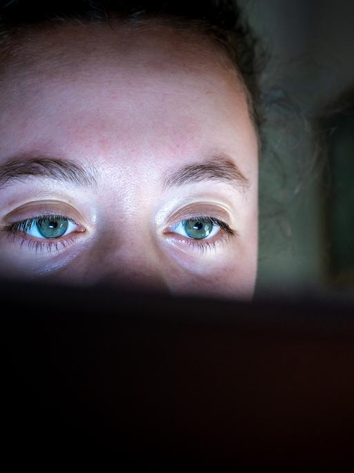 Nahaufnahme einer jungen Frau, die konzentriert auf einen Computerbildschirm schaut. Über dem Monitorrand sind ihre grünen Augen zu sehen.