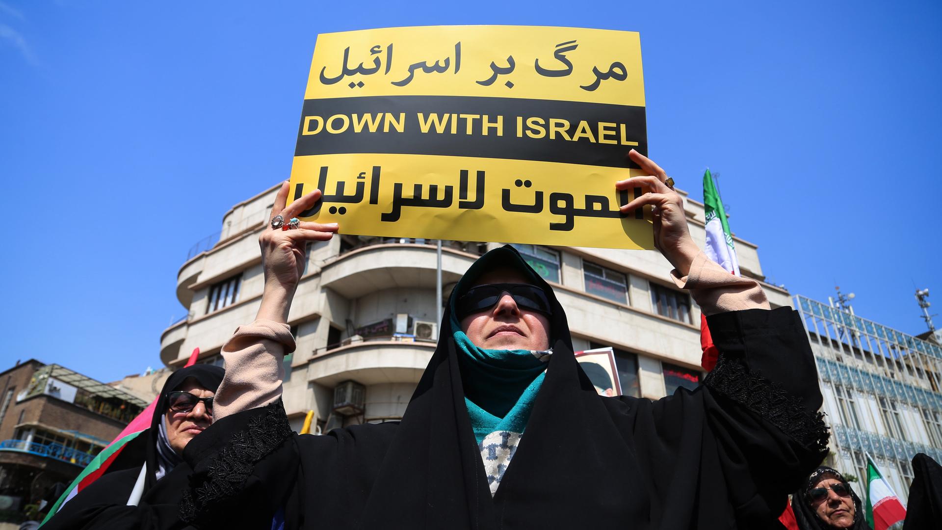 Eine verschleierte Frau hält bei anti-israelischen-Protesten in der iranischen Hauptstadt einen Zettel hoch. Darauf steht "Nieder mit Israel" in englischer und persischer Schrift. 